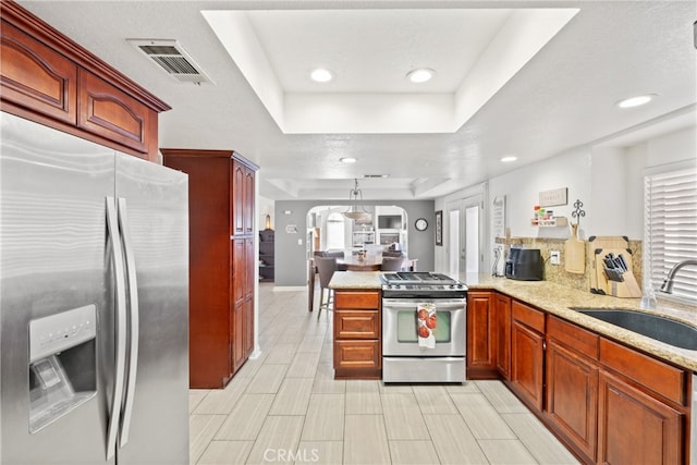 kitchen featuring sink, kitchen peninsula, stainless steel appliances, a raised ceiling, and decorative light fixtures