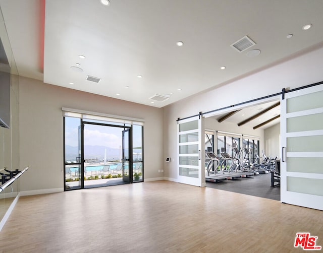 exercise room with hardwood / wood-style flooring, a barn door, and vaulted ceiling