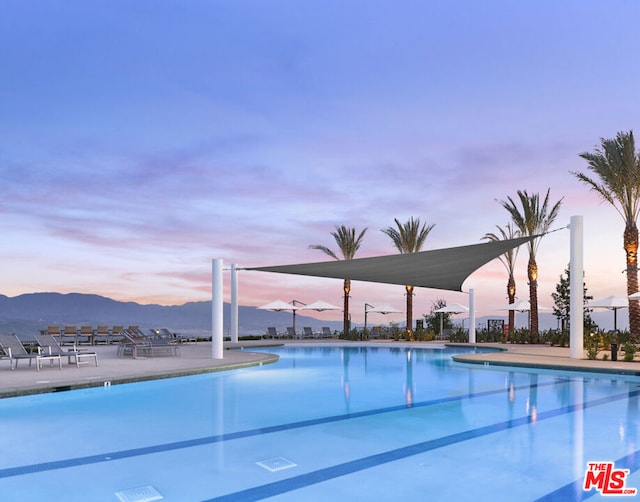 pool at dusk featuring a mountain view and a patio