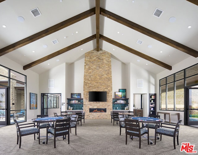 dining space with light carpet, beamed ceiling, a stone fireplace, and high vaulted ceiling