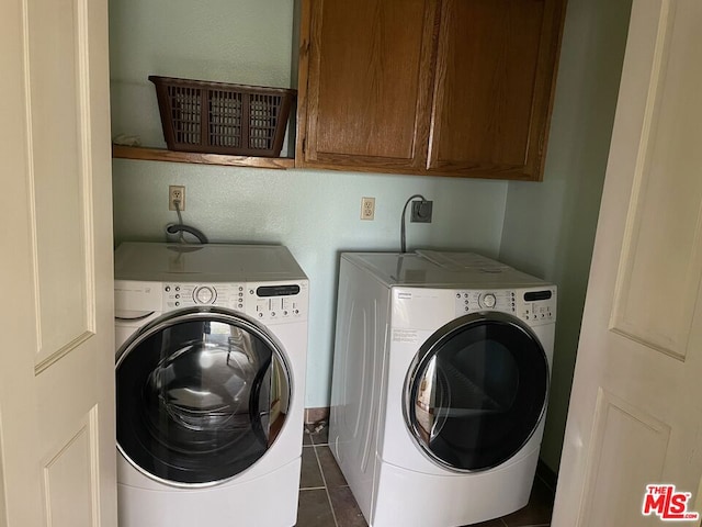 clothes washing area with washing machine and clothes dryer, dark tile patterned flooring, and cabinets