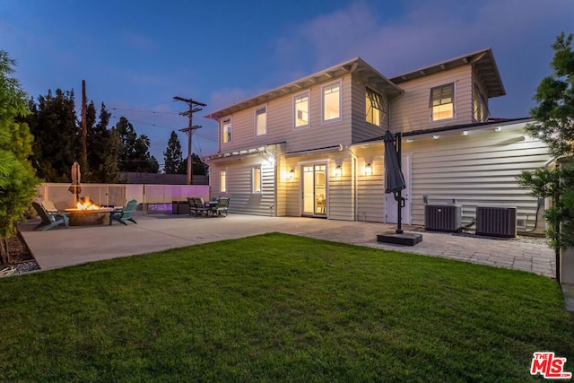 back house at dusk with a patio, a lawn, central AC unit, and an outdoor fire pit