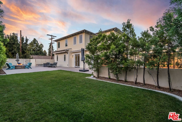 back house at dusk with a fire pit, a patio area, and a lawn