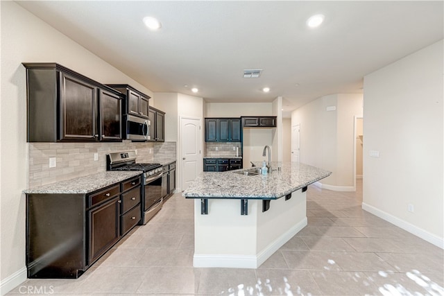 kitchen featuring appliances with stainless steel finishes, light stone countertops, sink, and an island with sink