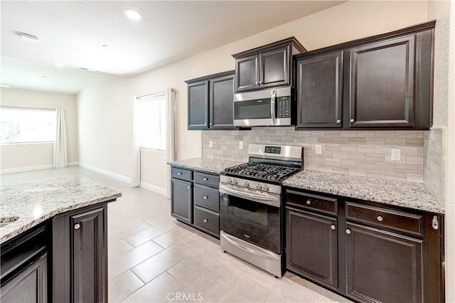 kitchen featuring dark brown cabinets, light stone countertops, stainless steel appliances, and backsplash