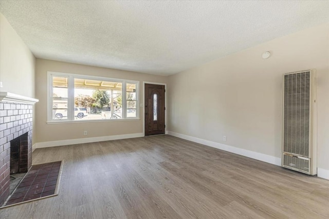 unfurnished living room with a textured ceiling, light hardwood / wood-style floors, and a brick fireplace