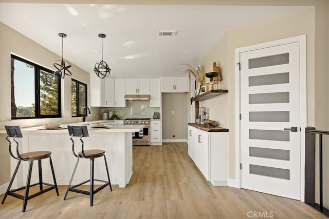 kitchen with a breakfast bar, white cabinets, stainless steel stove, light wood-type flooring, and decorative light fixtures