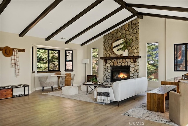 living room with light hardwood / wood-style flooring, beam ceiling, high vaulted ceiling, and a stone fireplace