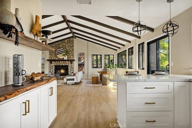 kitchen featuring decorative light fixtures, white cabinetry, a fireplace, lofted ceiling with beams, and light wood-type flooring