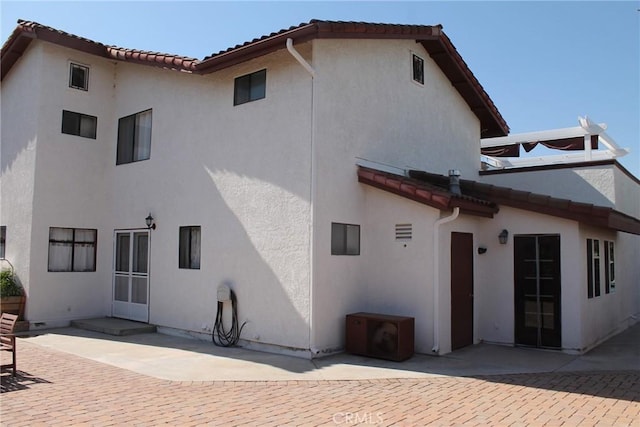 rear view of property featuring stucco siding, a patio area, and a tile roof