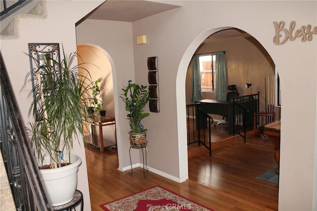 corridor featuring arched walkways, baseboards, and wood finished floors