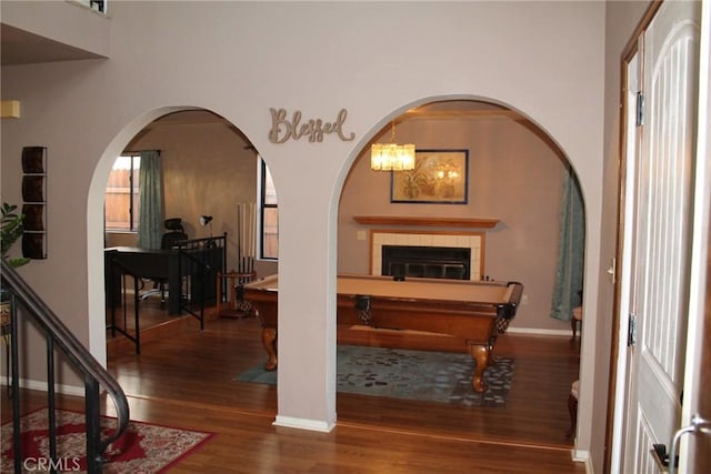 recreation room featuring baseboards, a fireplace, arched walkways, and wood finished floors
