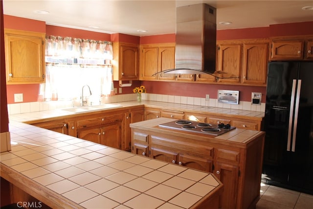 kitchen featuring island exhaust hood, black fridge, tile countertops, stainless steel gas cooktop, and sink