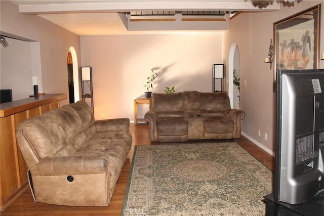 living room with arched walkways, wood finished floors, and beamed ceiling