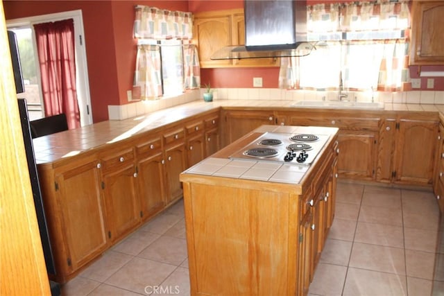 kitchen featuring light tile patterned flooring, tile countertops, wall chimney exhaust hood, stainless steel electric cooktop, and a sink