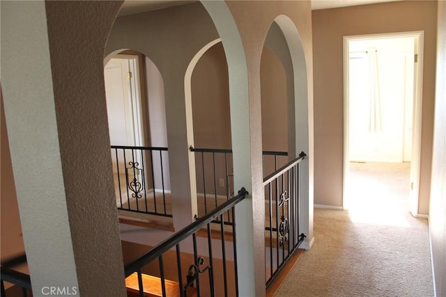 hallway with carpet floors, arched walkways, and an upstairs landing