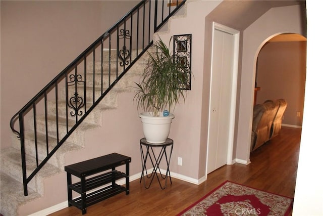 stairway featuring arched walkways, baseboards, and wood finished floors