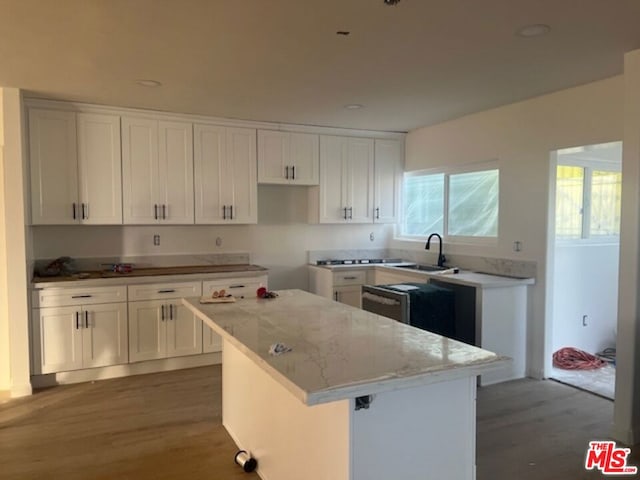 kitchen with light stone counters, sink, a kitchen island, white cabinetry, and hardwood / wood-style flooring