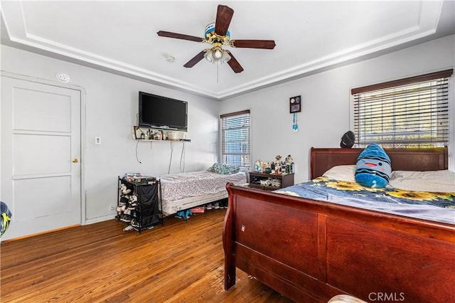 bedroom with wood-type flooring, a tray ceiling, and ceiling fan