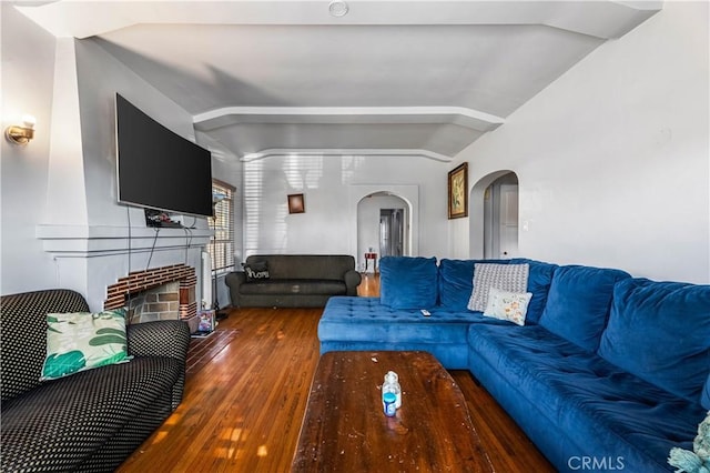 living room featuring dark hardwood / wood-style floors, lofted ceiling, and a brick fireplace