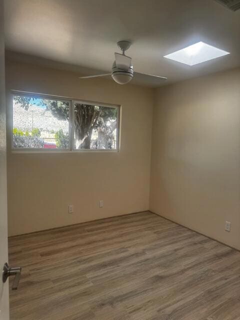 unfurnished room with ceiling fan, wood-type flooring, and a skylight