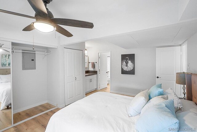 bedroom featuring ensuite bath, ceiling fan, electric panel, and light wood-type flooring