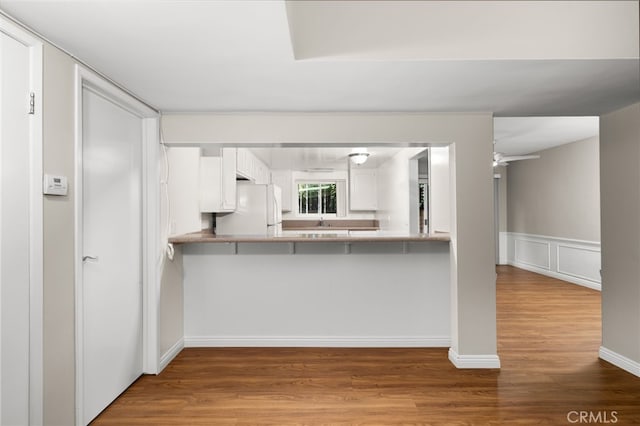 kitchen with white fridge, hardwood / wood-style floors, a breakfast bar, kitchen peninsula, and white cabinetry