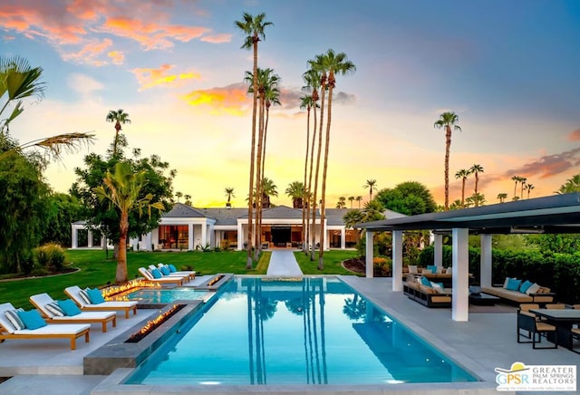 pool at dusk with outdoor lounge area, a patio area, a yard, and a jacuzzi