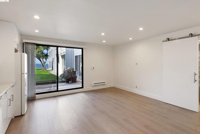 empty room featuring a barn door, baseboard heating, and light hardwood / wood-style floors