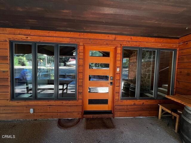 doorway to outside with carpet, wood ceiling, and wood walls