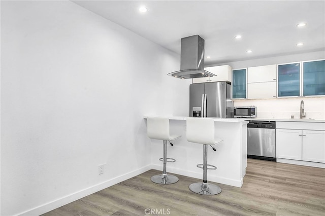 kitchen with white cabinets, sink, island exhaust hood, stainless steel appliances, and a breakfast bar area