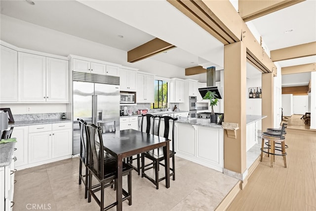 kitchen with white cabinets, light stone counters, appliances with stainless steel finishes, and extractor fan