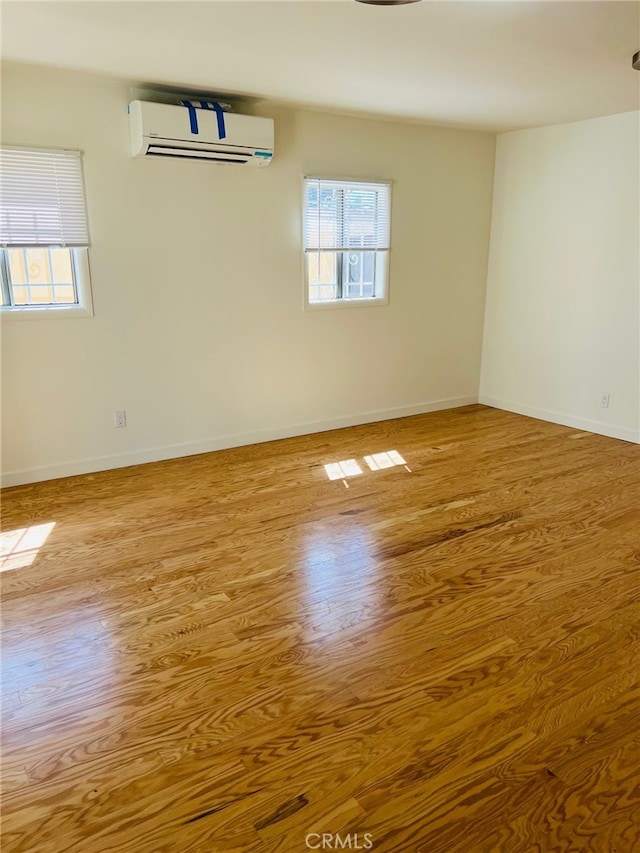 empty room with a wall mounted air conditioner, plenty of natural light, and light hardwood / wood-style floors