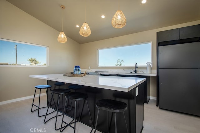 kitchen featuring sink, vaulted ceiling, a kitchen breakfast bar, decorative light fixtures, and stainless steel fridge