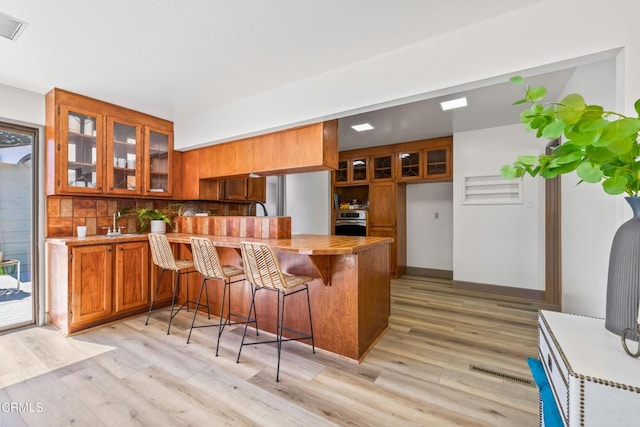 kitchen featuring a breakfast bar, oven, decorative backsplash, light hardwood / wood-style floors, and kitchen peninsula