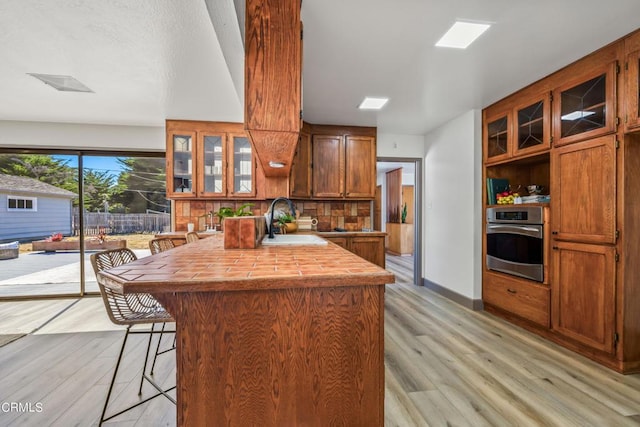 kitchen with a breakfast bar, stainless steel oven, backsplash, sink, and light hardwood / wood-style floors