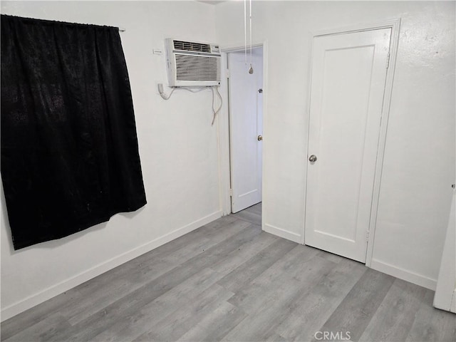 unfurnished bedroom featuring light wood-type flooring and an AC wall unit