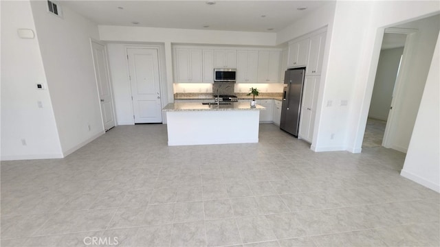 kitchen with light tile patterned floors, a center island with sink, white cabinetry, appliances with stainless steel finishes, and light stone countertops