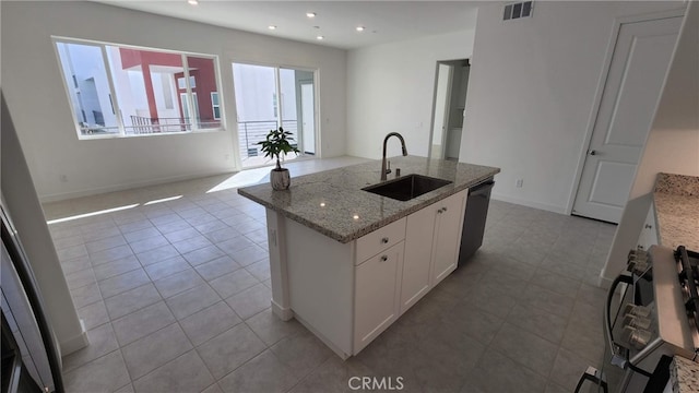 kitchen with light tile patterned flooring, sink, white cabinetry, stone counters, and a center island with sink