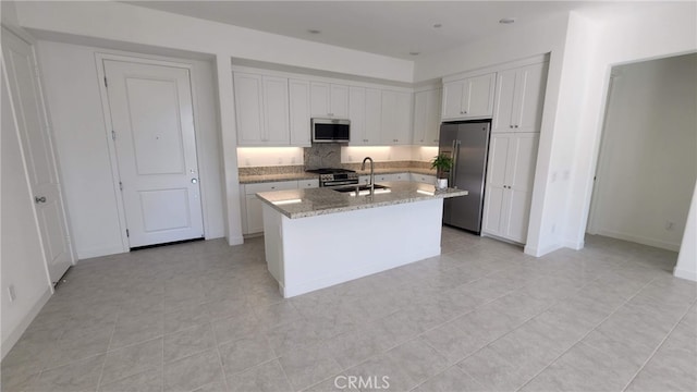 kitchen featuring sink, a kitchen island with sink, white cabinetry, stainless steel appliances, and light stone countertops