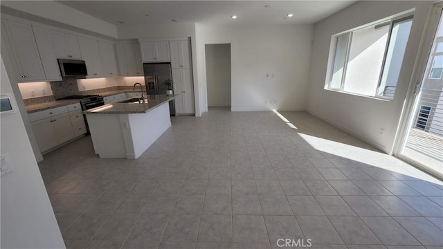 kitchen with dark stone counters, a kitchen island with sink, sink, white cabinets, and fridge with ice dispenser