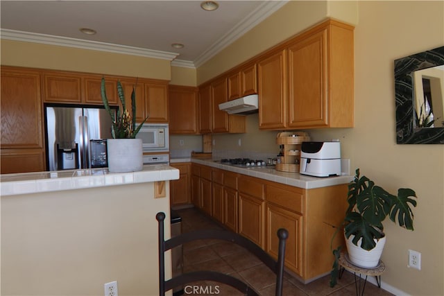 kitchen with stainless steel fridge, dark tile patterned flooring, tile countertops, crown molding, and gas cooktop