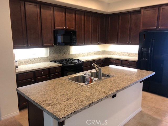 kitchen with black appliances, a center island with sink, sink, and light stone counters