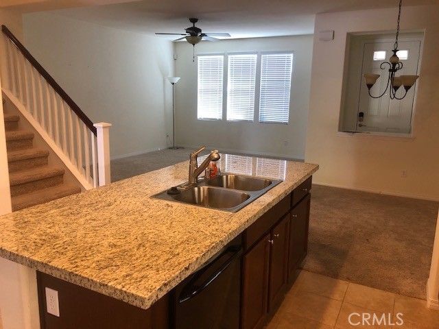 kitchen featuring dishwasher, a kitchen island with sink, sink, ceiling fan with notable chandelier, and light colored carpet