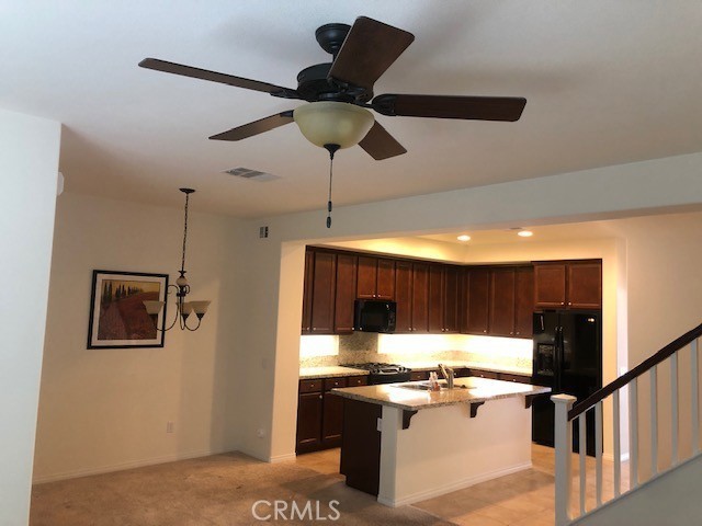 kitchen featuring sink, an island with sink, a kitchen breakfast bar, black appliances, and ceiling fan