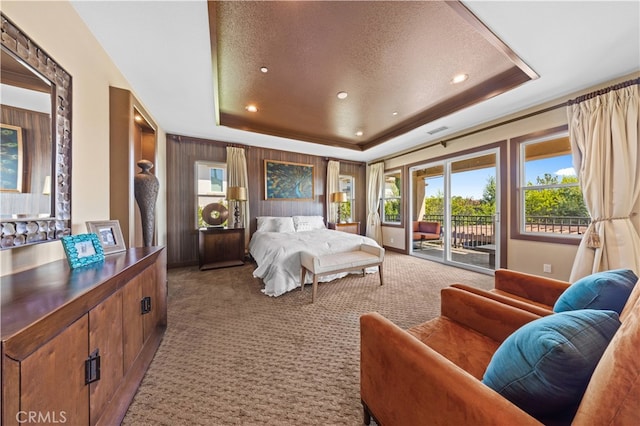 carpeted bedroom with a textured ceiling, a raised ceiling, and access to exterior