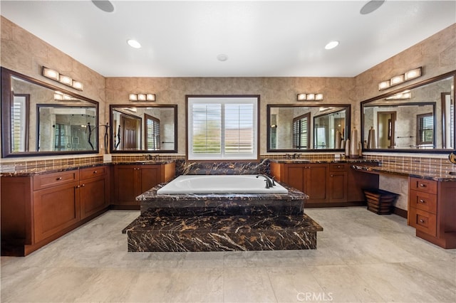 bathroom featuring a relaxing tiled tub, vanity, and tile walls