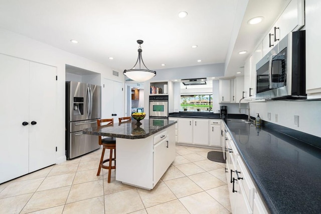 kitchen featuring a kitchen island, decorative light fixtures, white cabinetry, appliances with stainless steel finishes, and a breakfast bar