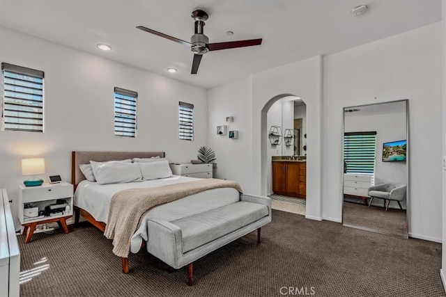 carpeted bedroom with ensuite bathroom, multiple windows, and ceiling fan