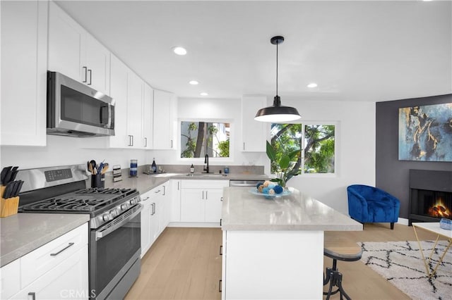 kitchen with white cabinets, decorative light fixtures, stainless steel appliances, and light hardwood / wood-style flooring